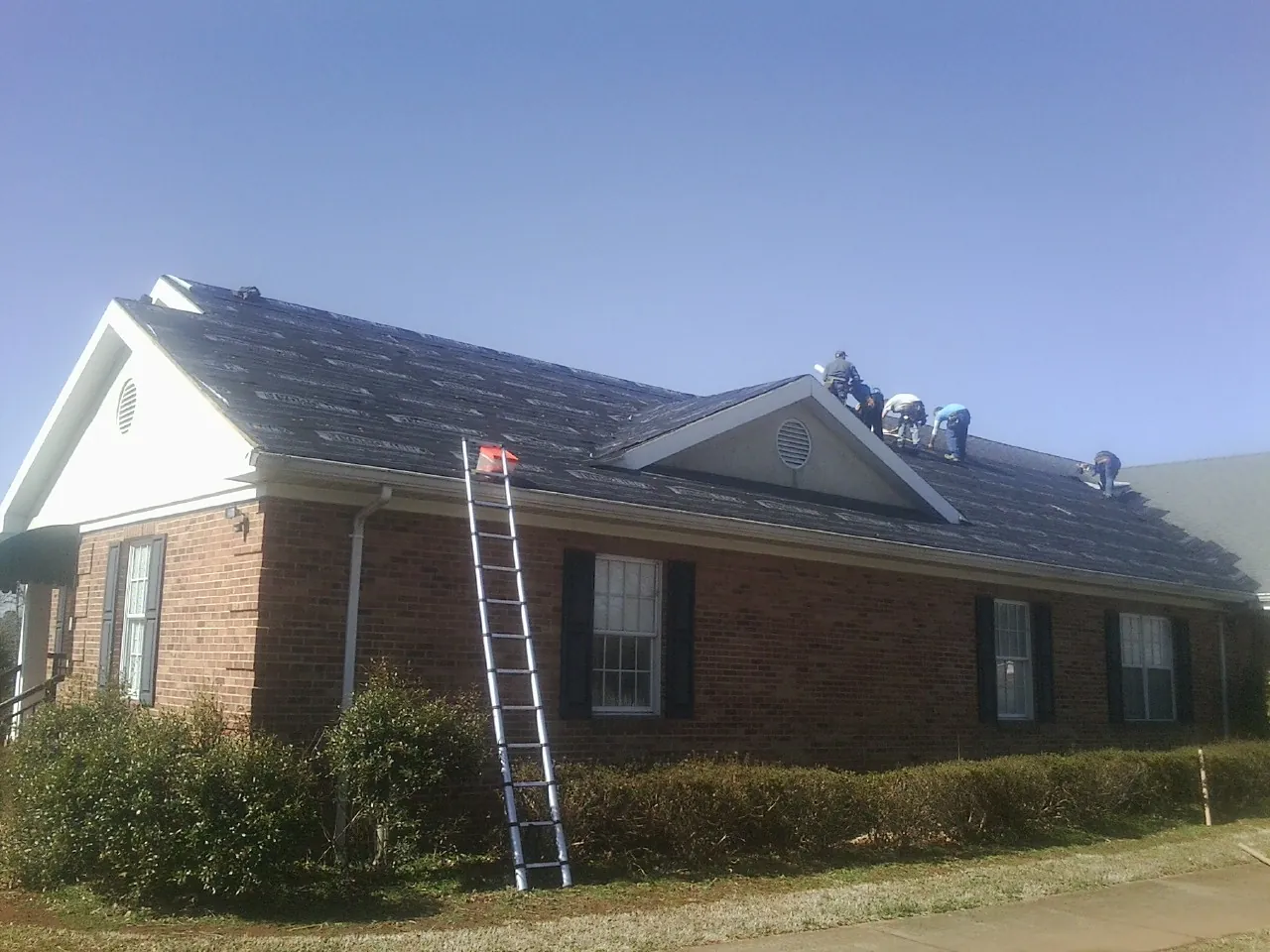 Crew tearing shingles off a brick ranch roof with a ladder set — Emergency Roof Repair work by our crew in Pomfret
