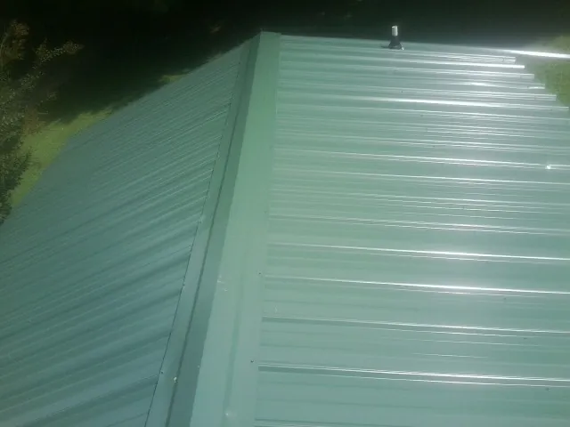 New green metal panels meeting at the ridge of a roof — Flat Roof Repair work by our crew in Pomfret